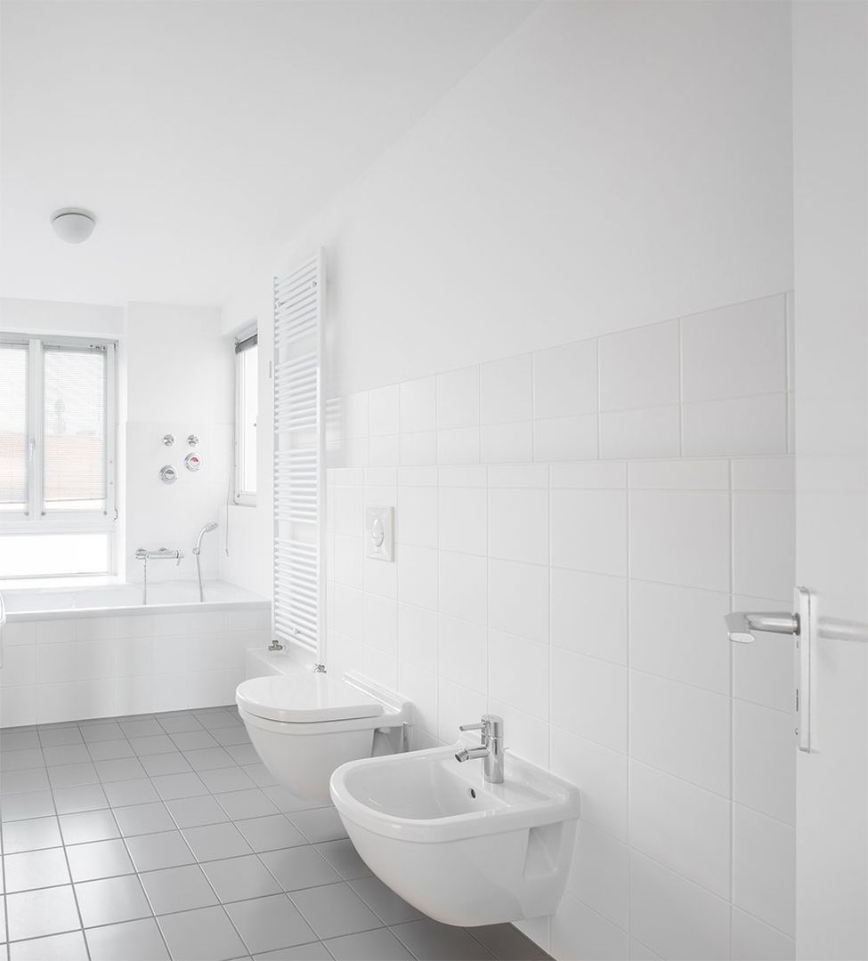 Minimalistisches Badezimmer mit weißen Wänden, einer Badewanne und zwei weißen Bidets